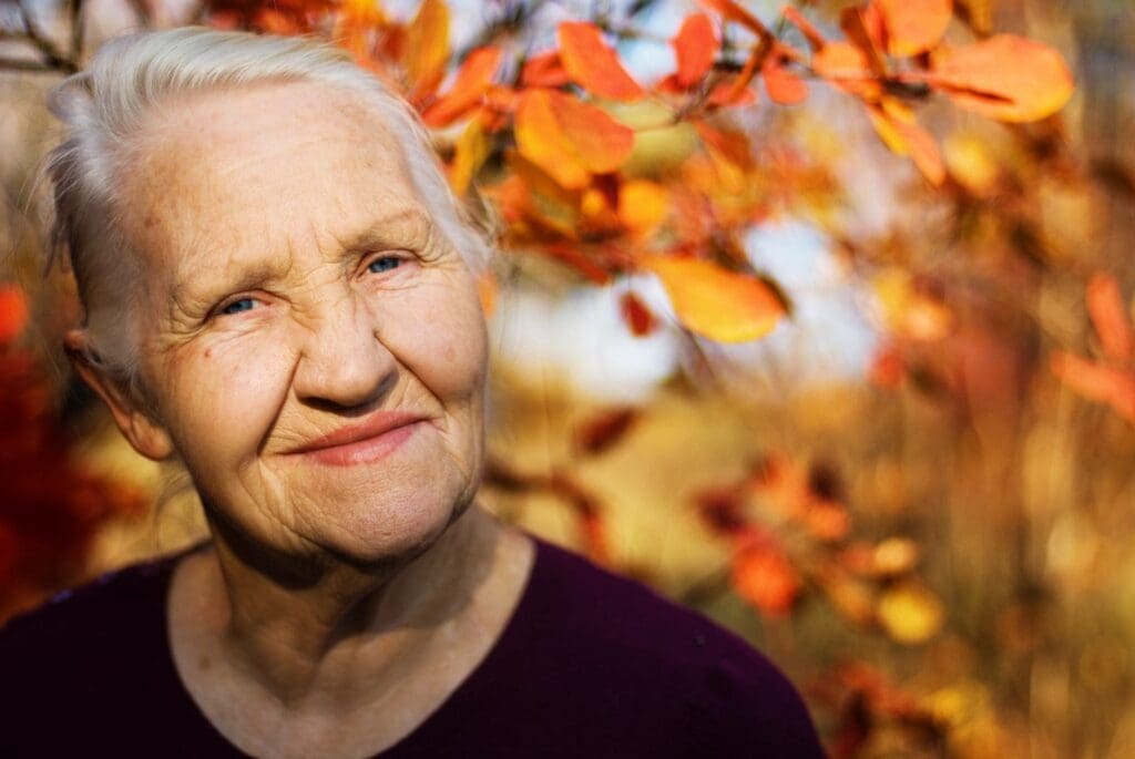 Older woman with grey hair standing in front of orange leaves